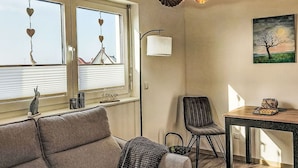 A cozy room with a sofa, a table with a plate of food, a chair, a lamp, and a painting of a tree. - Cosy apartment for 2 people with WIFI, TV and terrace (Schieder-schwalenberg)