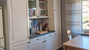 A kitchen with white cabinetry, a wooden table, and a window with striped curtains. - Cosy apartment for 2 guests with WIFI, TV and terrace (Stadtoldendorf)