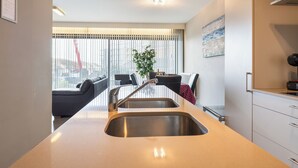 A modern kitchen with a built-in sink, a dining area with a black sofa and a table, and a large window with blinds. - 1 bedroom accommodation in Sint-Idesbald (Sint-Idesbald)