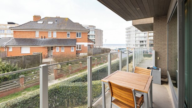 A balcony with a wooden table and chairs, overlooking a residential area and the sea. - 1 bedroom accommodation in Sint-Idesbald (Sint-Idesbald)