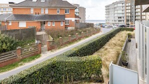 A residential area with a brick house, a wooden fence, and a road leading to a modern building with a balcony. - 1 bedroom accommodation in Sint-Idesbald (Sint-Idesbald)