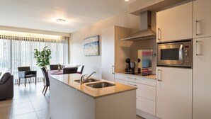 A modern kitchen with a central island, stainless steel appliances, and a dining area with a plant and chairs. - 1 bedroom accommodation in Sint-Idesbald (Sint-Idesbald)