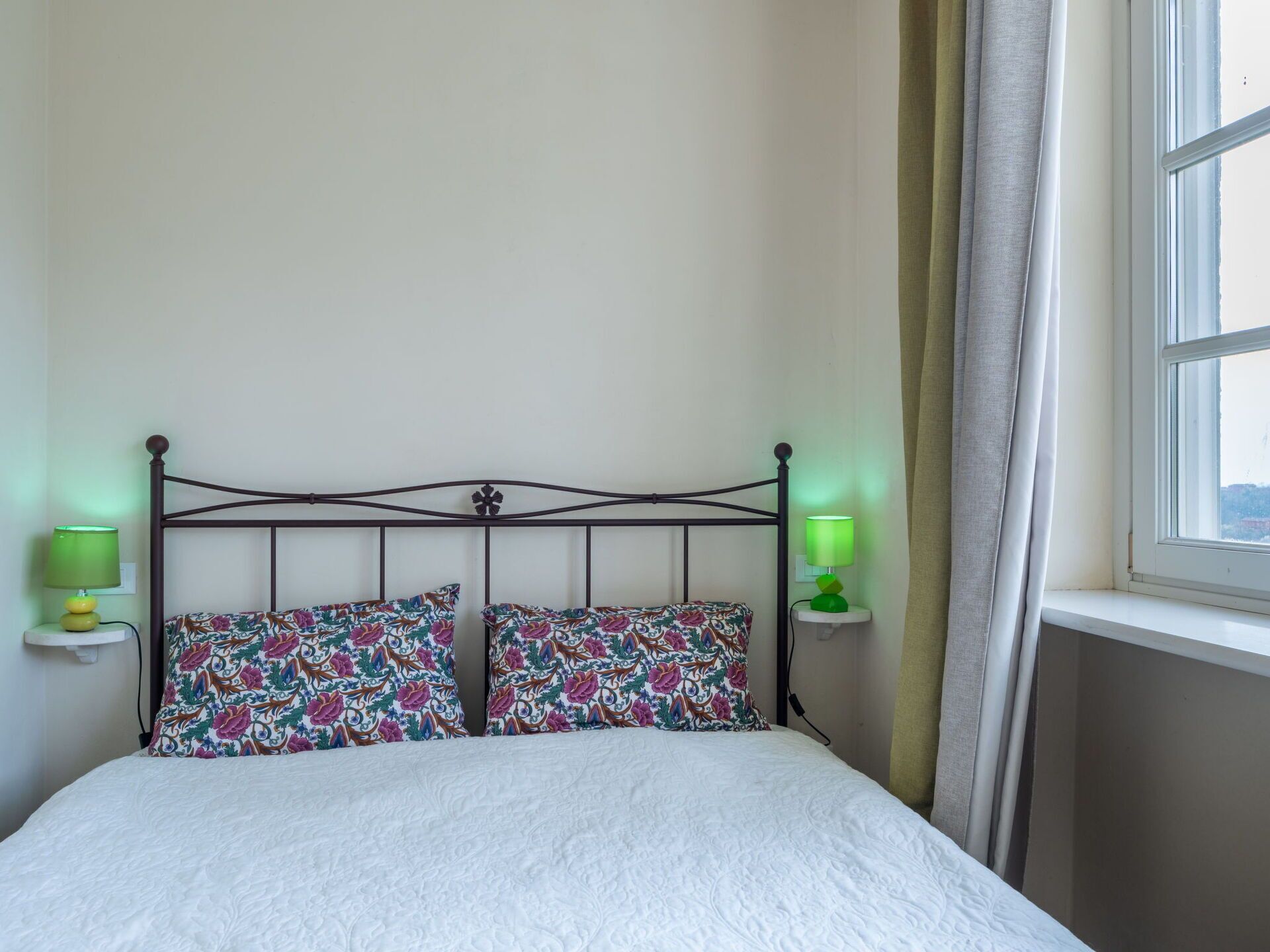 A bed with floral-patterned pillows, a white duvet, and two bedside lamps.