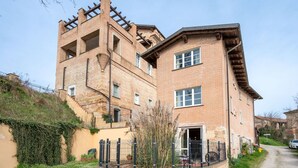 Un immeuble en briques à plusieurs étages, doté d’une tour imposante, d’un escalier menant aux étages supérieurs et d’un espace extérieur clôturé avec une table et des chaises.