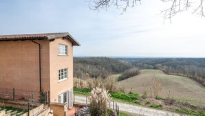 Un bâtiment en briques avec un toit plat, une terrasse entourée d’une clôture et une vue sur un paysage vallonné.