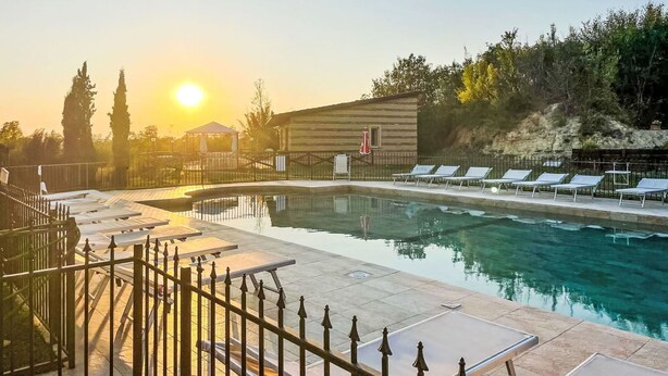 Une piscine avec des chaises longues, une clôture et un bâtiment en arrière-plan.