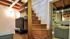 Un espace de vie compact comprenant un escalier en bois, un téléviseur posé sur un meuble en bois, et une salle de bain avec un lavabo et un miroir.