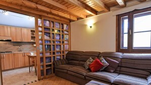 Un salon chaleureux avec un plafond en bois, un canapé agrémenté de coussins à rayures, une petite table et, au fond, une cuisine.