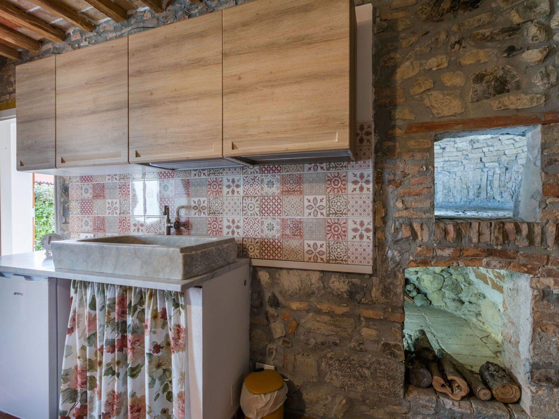 A kitchen with wooden cabinets, a tiled backsplash, and a stone wall.