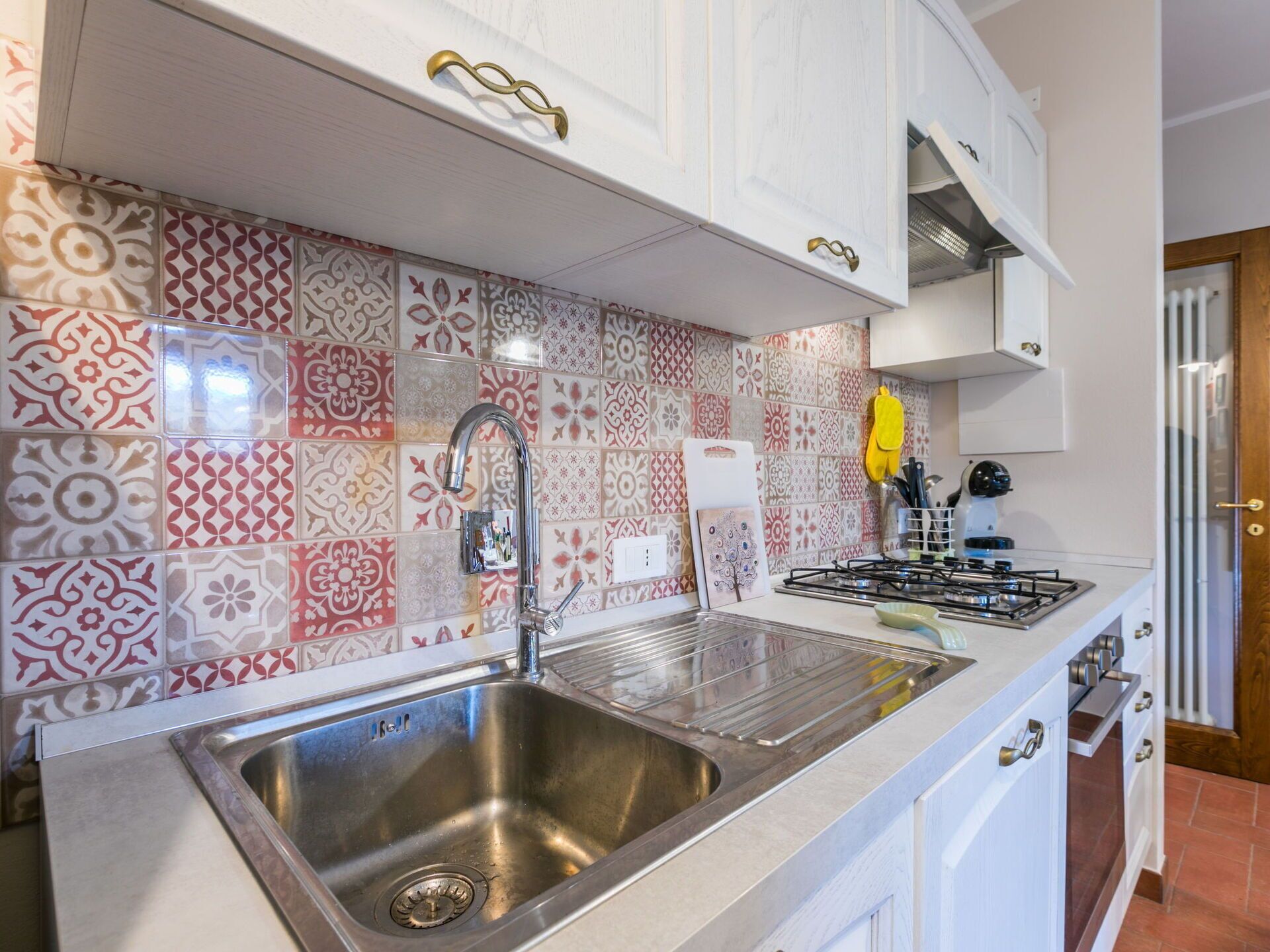 Una cocina con baldosas estampadas, pileta de acero inoxidable y muebles blancos.