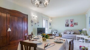 A dining area with a table set for two, a wooden cabinet, and a sofa in the background.
