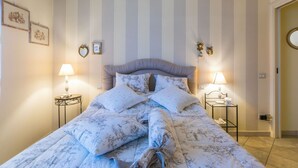 A neatly made bed with floral bedding, two bedside tables with lamps, and a striped wall with framed pictures.