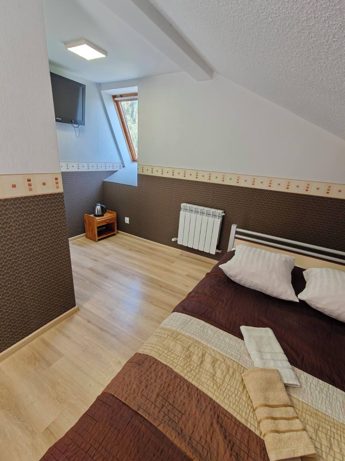 A bedroom with a bed, a nightstand, a radiator, and a window.