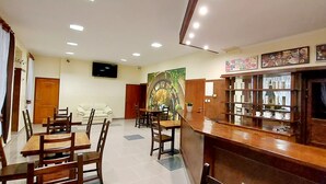 A hotel dining area with multiple wooden tables and chairs, a bar area with shelves of glasses and bottles, and a large mural on the wall. - Zajazd Panorama (Radymno)