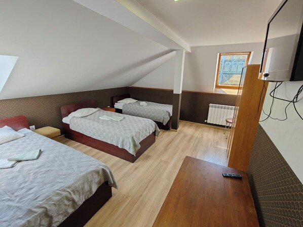 Una habitación con dos camas, una mesa de madera, un radiador y una ventana con vistas.