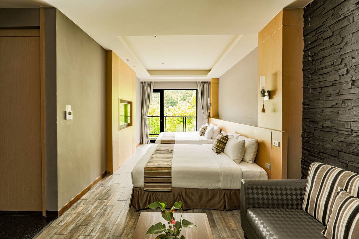 Une chambre d’hôtel avec deux lits, un canapé, une table basse et une vue sur la verdure environnante.