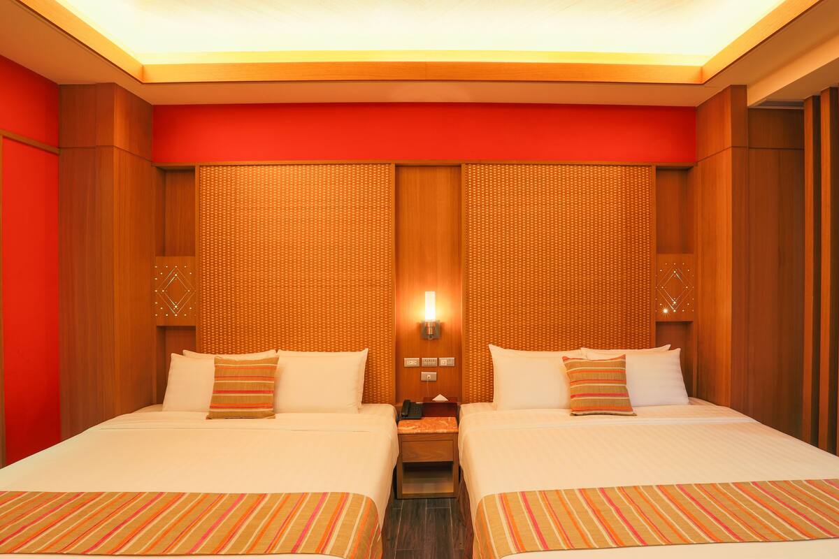 Une chambre d’hôtel avec deux lits, une tête de lit en bois, une lampe fixée au mur et une petite table de chevet.