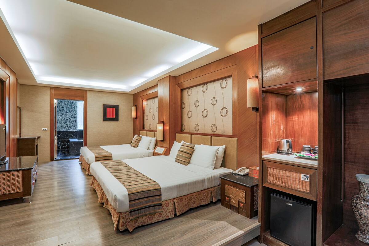Une chambre d’hôtel avec deux lits, un minibar, un petit réfrigérateur et une salle de bain avec douche et toilettes.