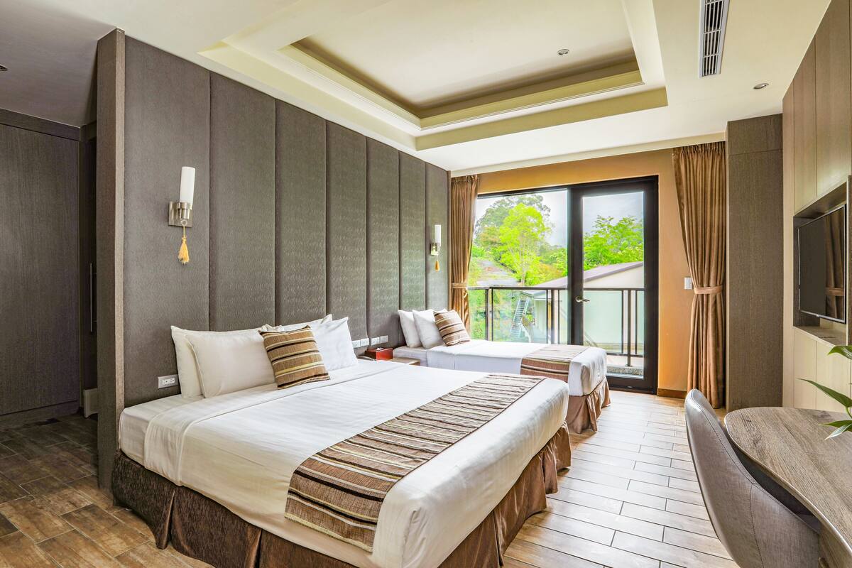 Une chambre d’hôtel avec un grand lit, un deuxième lit, un balcon avec vue, une télévision et un bureau.