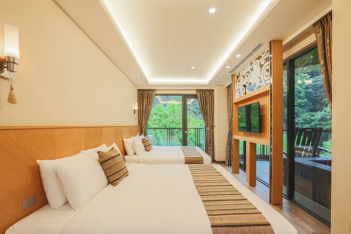 Une chambre d’hôtel avec deux lits, une télévision et un balcon donnant sur un espace verdoyant.
