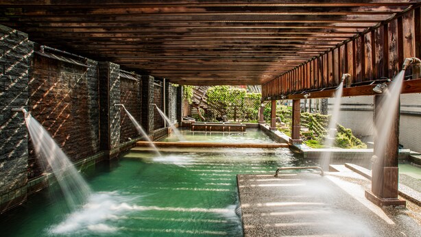 A spa area with a wooden ceiling, a stone wall, and a pool with water jets. - Sunrise Hot Spring Hotel (Taian)