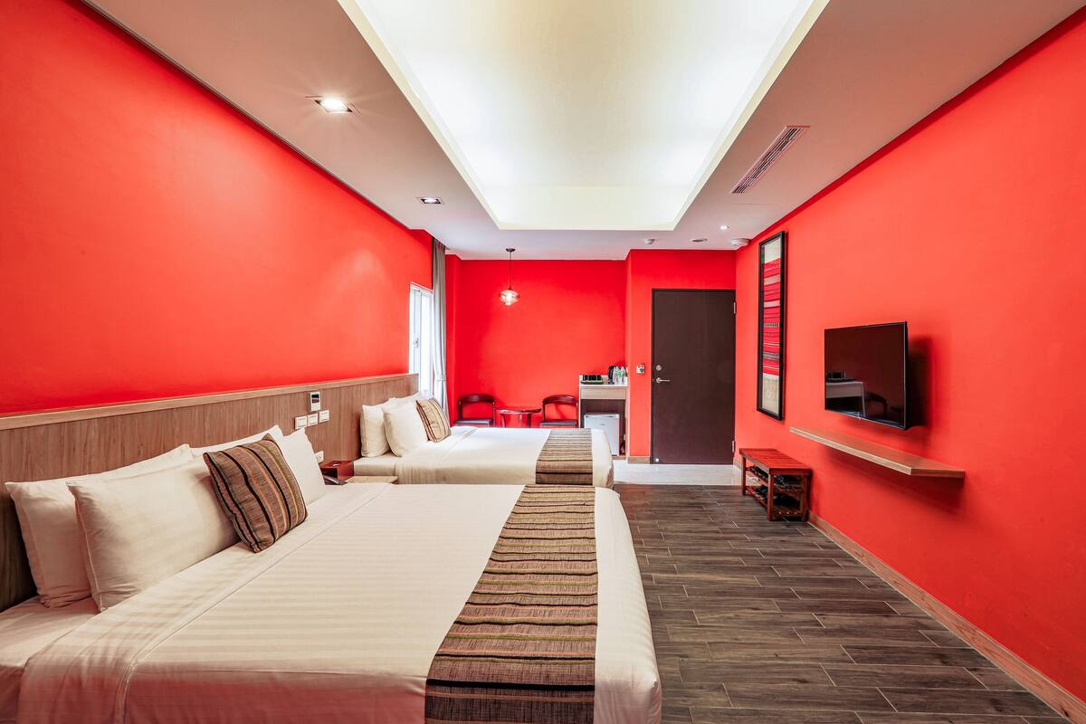 Une chambre d’hôtel avec deux lits, une télévision, un bureau et un mur rouge.