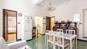 Una habitación de hotel compacta con kitchenette, un comedor con mesa y sillas, una cama y una araña.