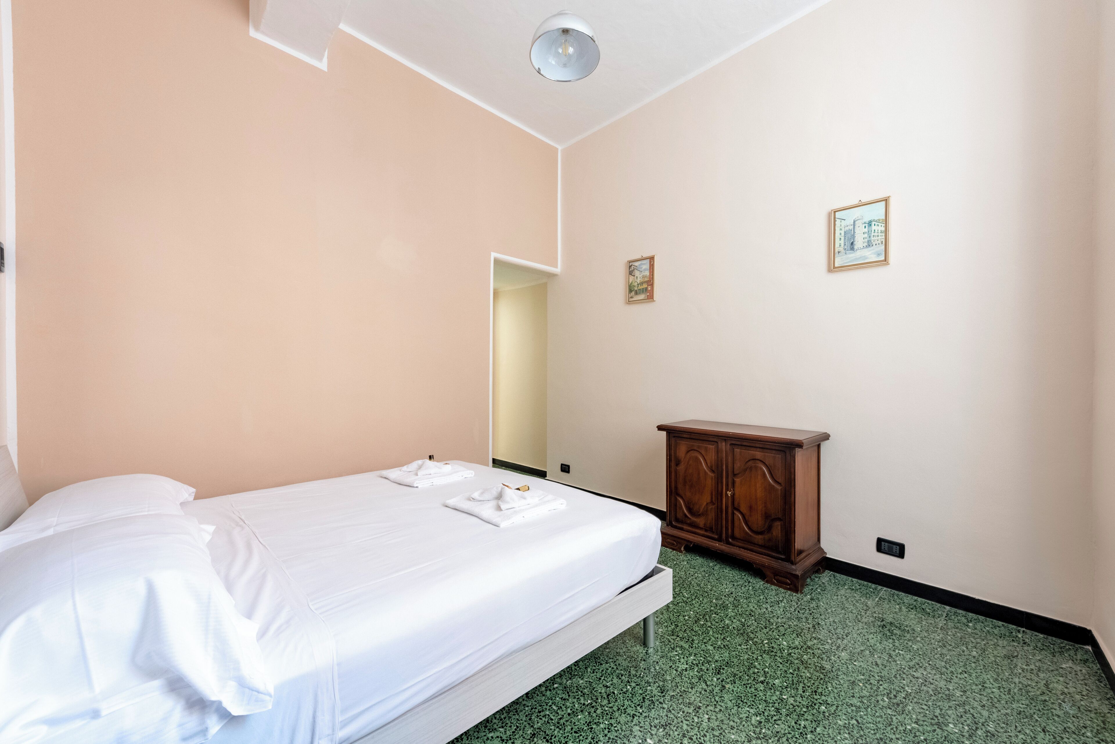 A hotel room with a bed, a wooden cabinet, and two framed pictures on the wall.
