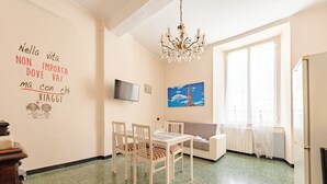 Una sala de estar acogedora con una mesa de comedor, sillas, un sofá, un televisor y un ventanal con cortinas.