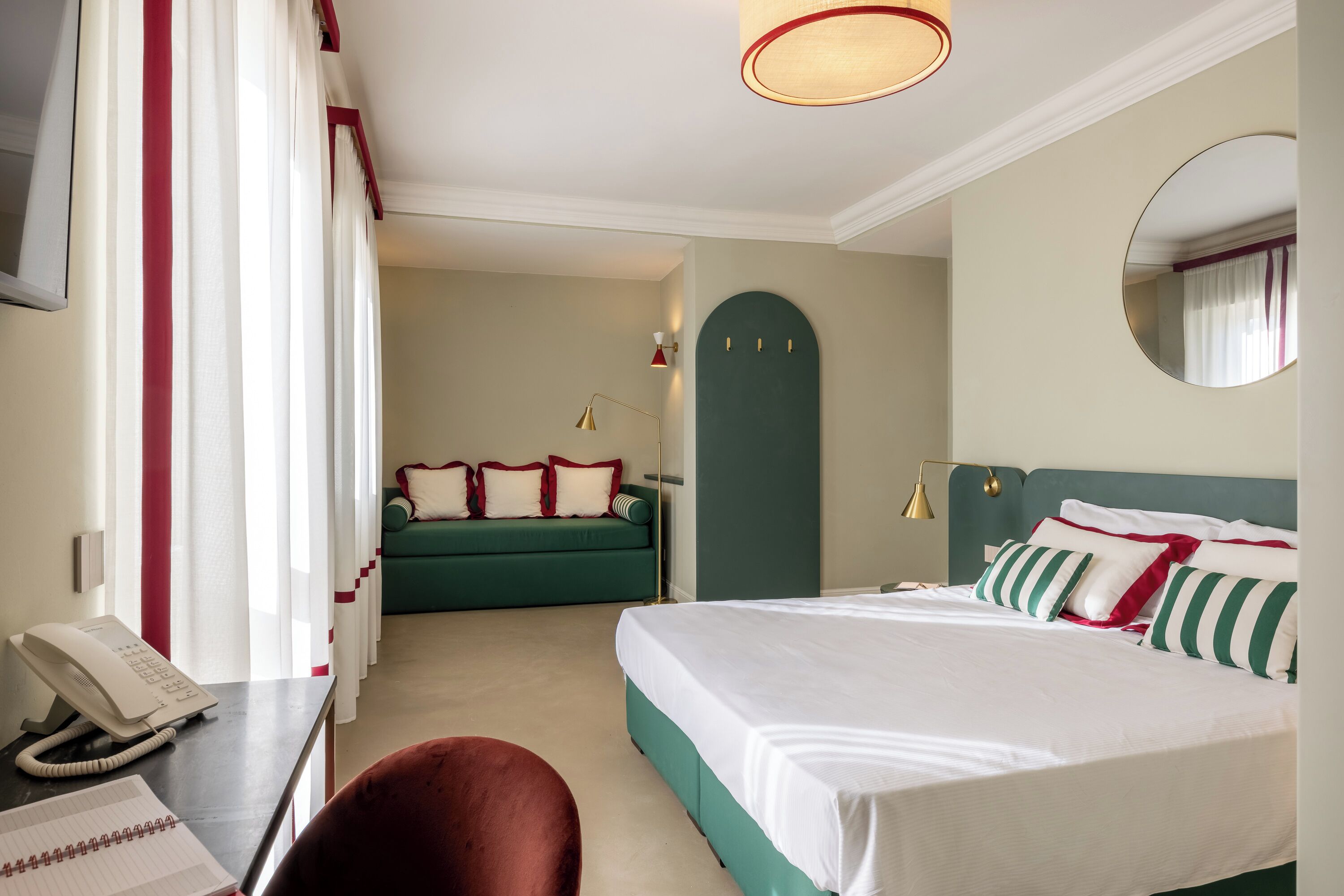 Una habitación de hotel con una cama, un escritorio con teléfono, un sofá verde y un espejo en la pared.