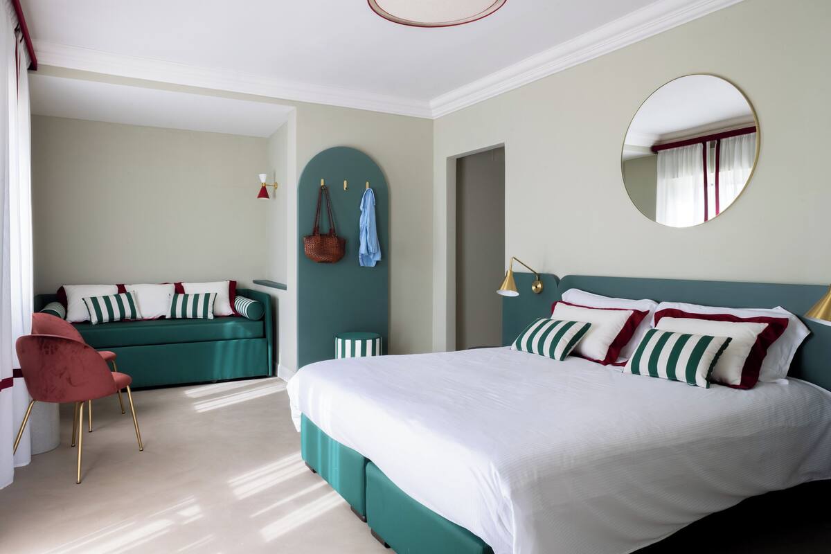 A bedroom with a large bed, a sofa, a chair, and a mirror on the wall.