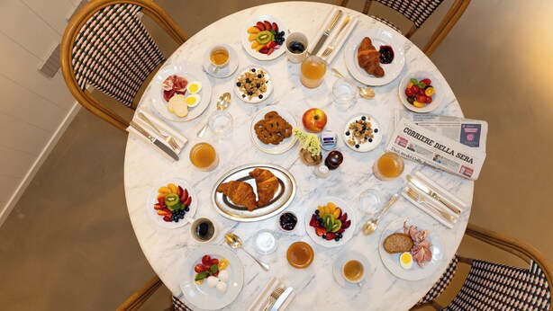 A round dining table with plates of food, cutlery, and a newspaper.