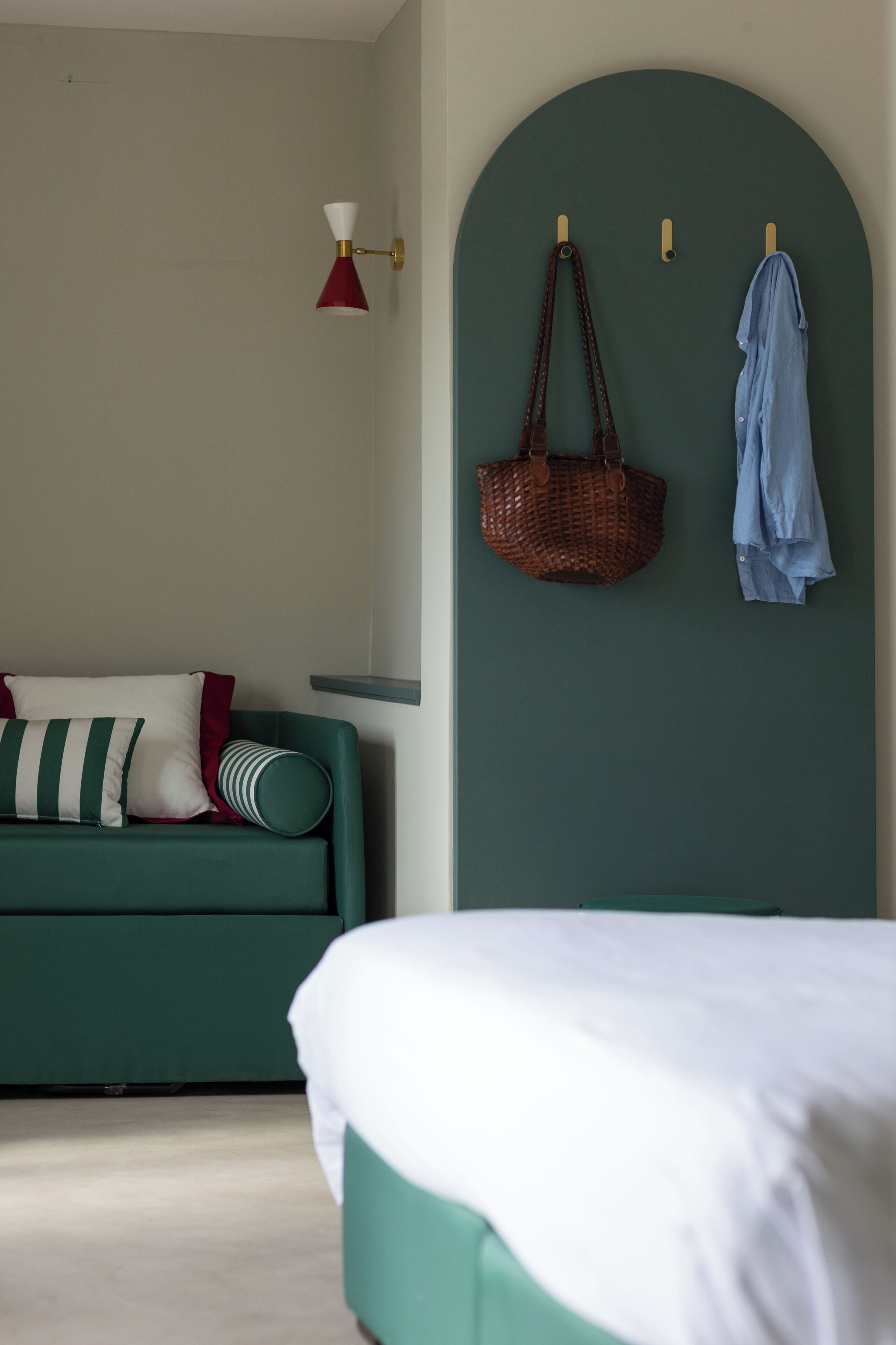Una habitación con un sofá verde, una cama, una lámpara de pared y un bolso colgando.
