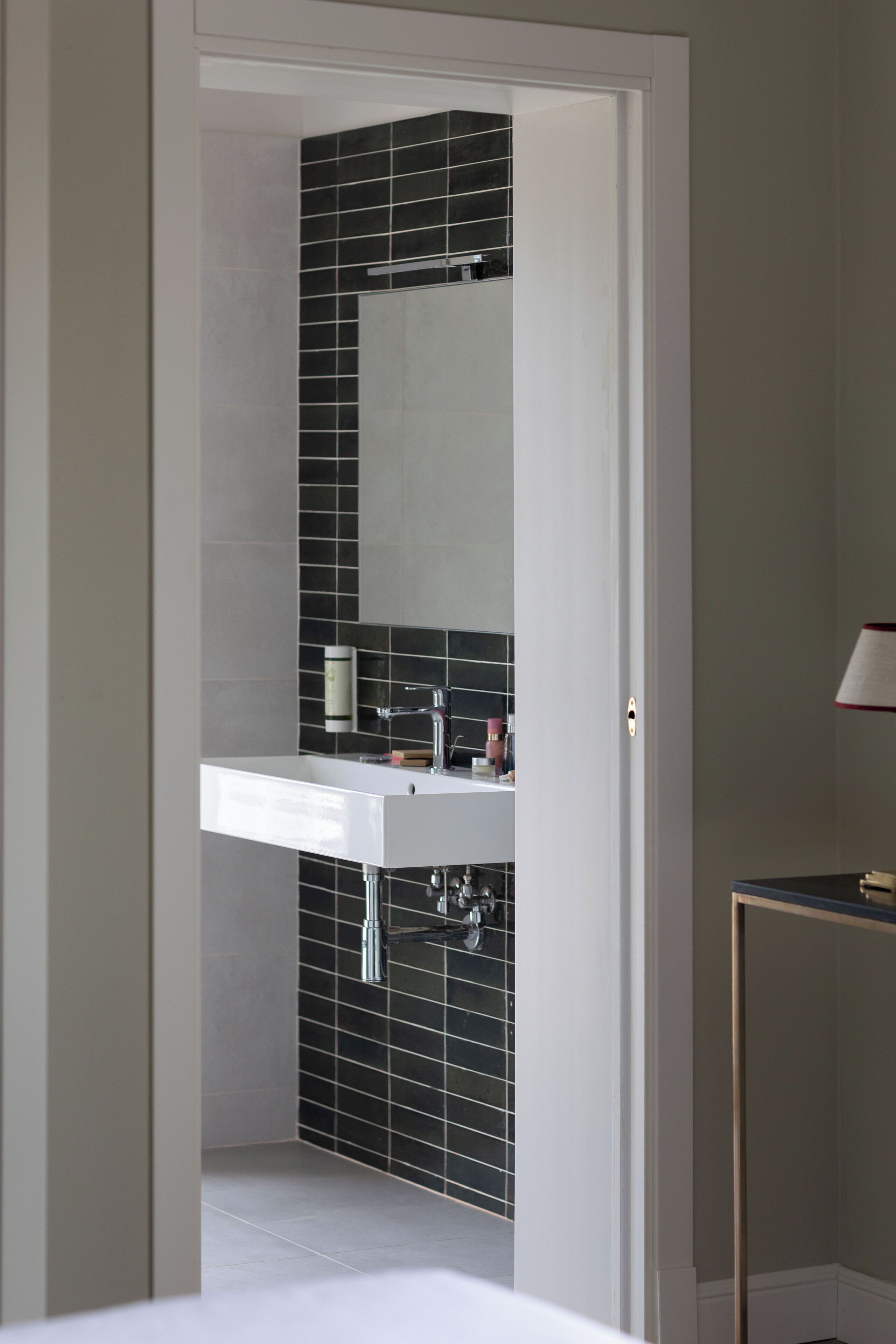 A bathroom with a white sink, black tiled walls, and a mirror.