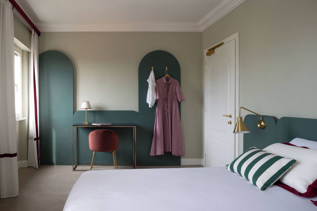 A bedroom with a bed, a desk, a chair, and a hanging coat rack.