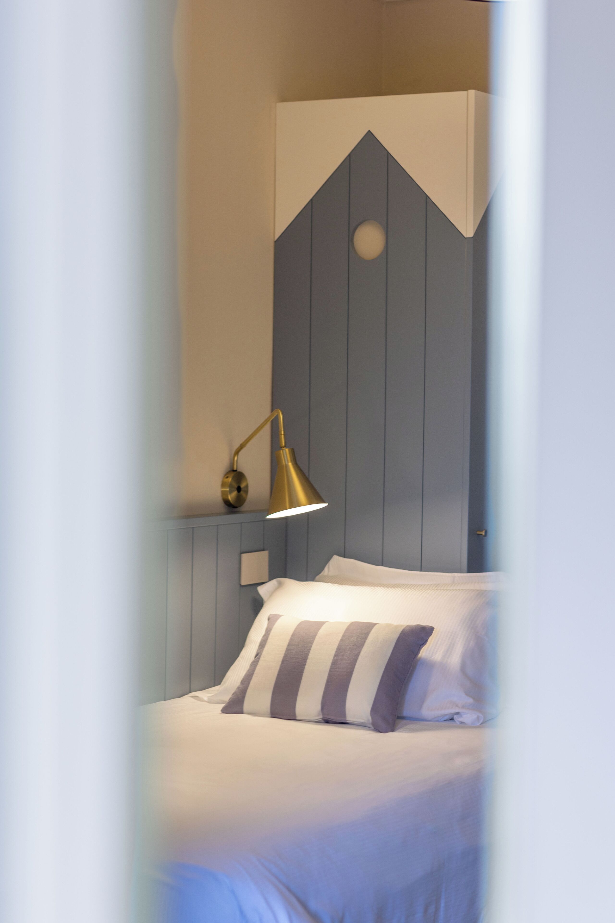 A neatly made bed with striped pillows, a wall-mounted lamp, and a simple, clean design.