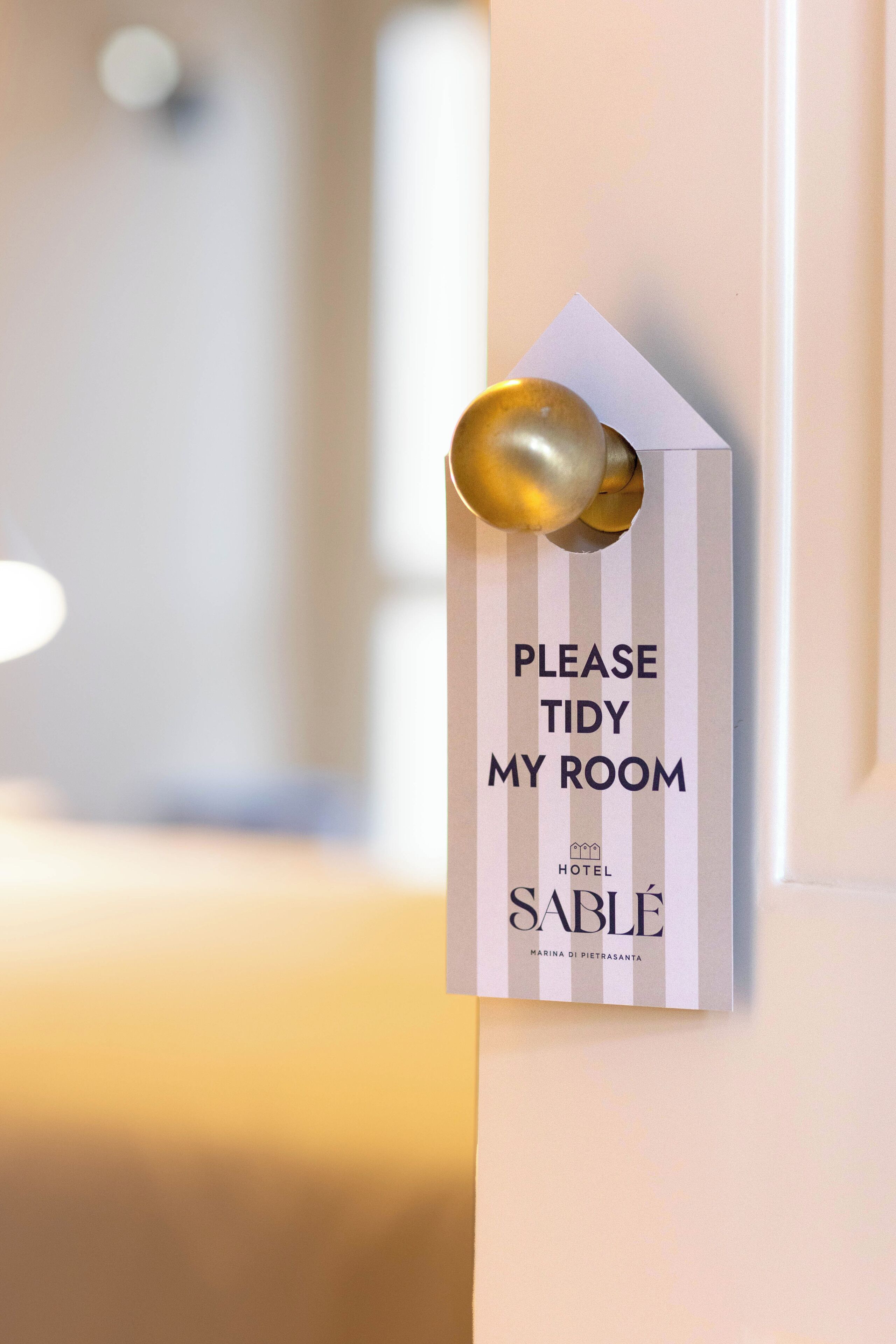 Un cartel en una puerta que dice: “POR FAVOR, ORDENA MI HABITACIÓN”, con el nombre del hotel “SABLE” y la ubicación “MARINA DI PIETRASANTA”.