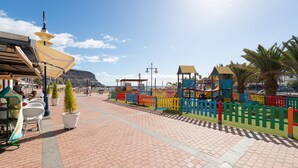 A paved walkway with colorful fences, a playground, and a mountain in the background. - House in Puerto de Mogan With Marina Views (Mogan)
