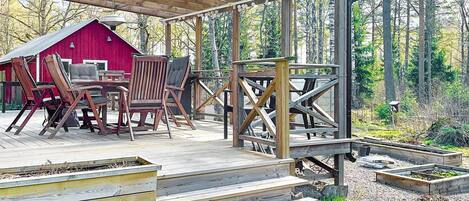 Una terraza de madera con mobiliario exterior, un granero rojo y un bosque de fondo.