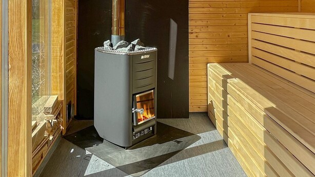 A wood-burning stove in a cabin with wooden walls, a bench, and a window. - 4 Star Holiday Home in Morlunda (Mörlunda)