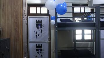A bunk bed room with a wooden wardrobe and a window with blinds.