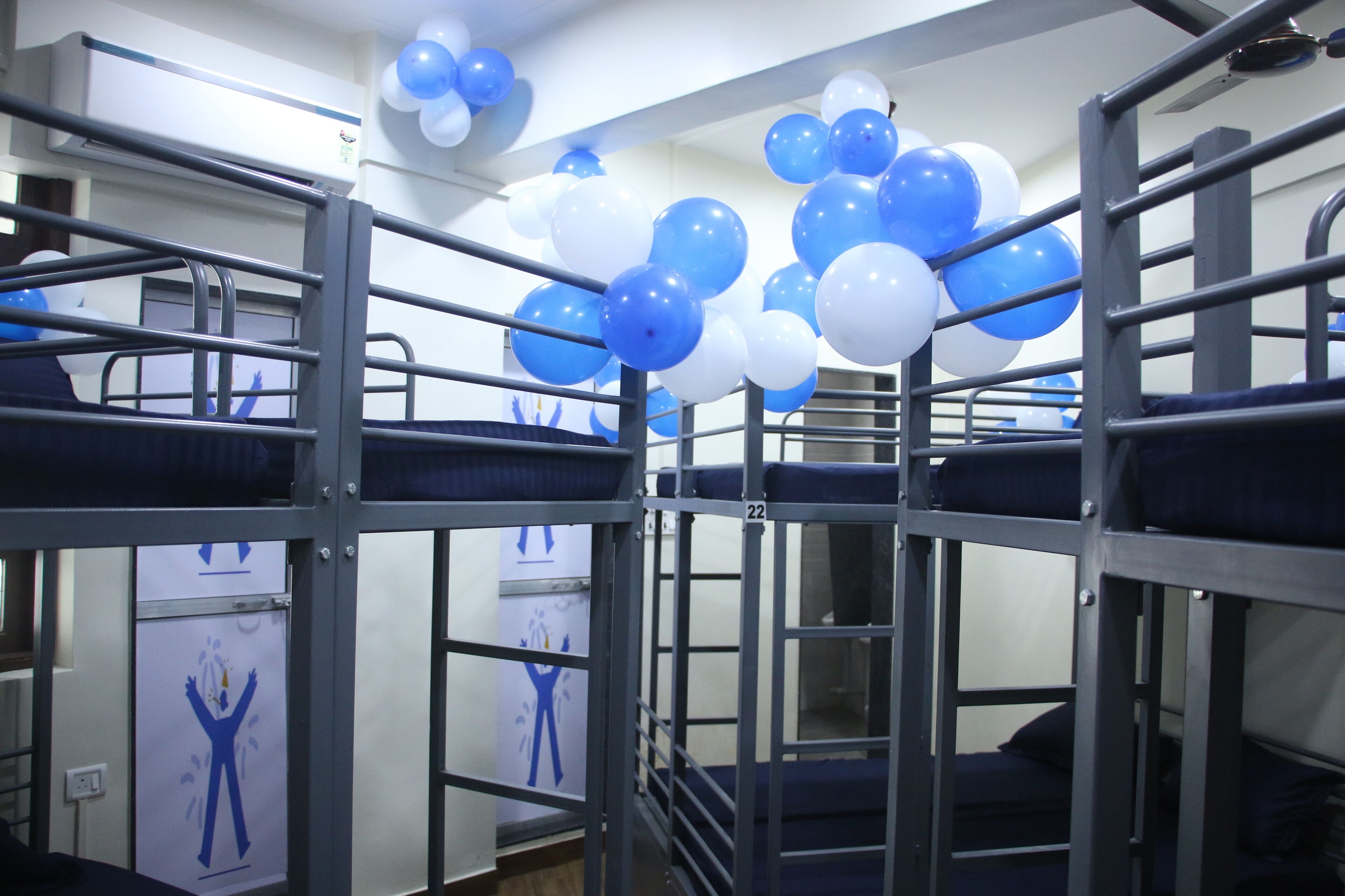 Bunk beds with blue and white balloons, a white air conditioning unit, and a door with a blue figure symbol.