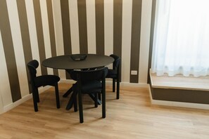 Un comedor con una mesa redonda y cuatro sillas, un cuenco negro pequeño sobre la mesa, y una ventana con cortina blanca.