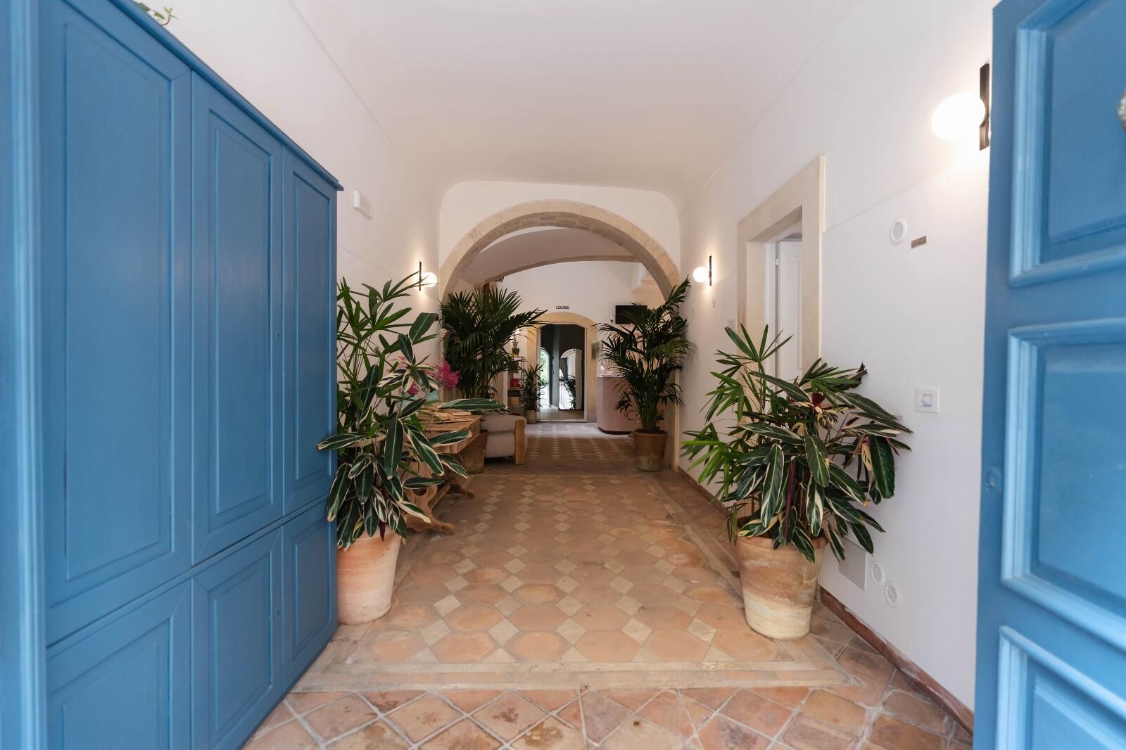 A hallway with blue doors, potted plants, and a tiled floor.