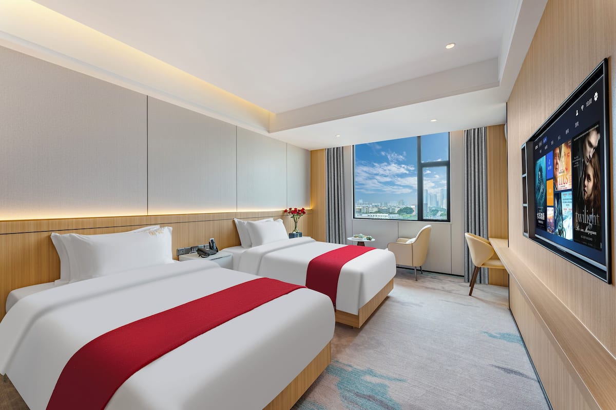 Hotelkamer met twee bedden, een televisie, uitzicht over de stad en een klein tafeltje met stoelen.