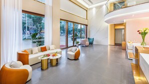 Een ruime lobby met een modern design, met een zithoek met banken en fauteuils, een receptiebalie en grote ramen met uitzicht op buiten.