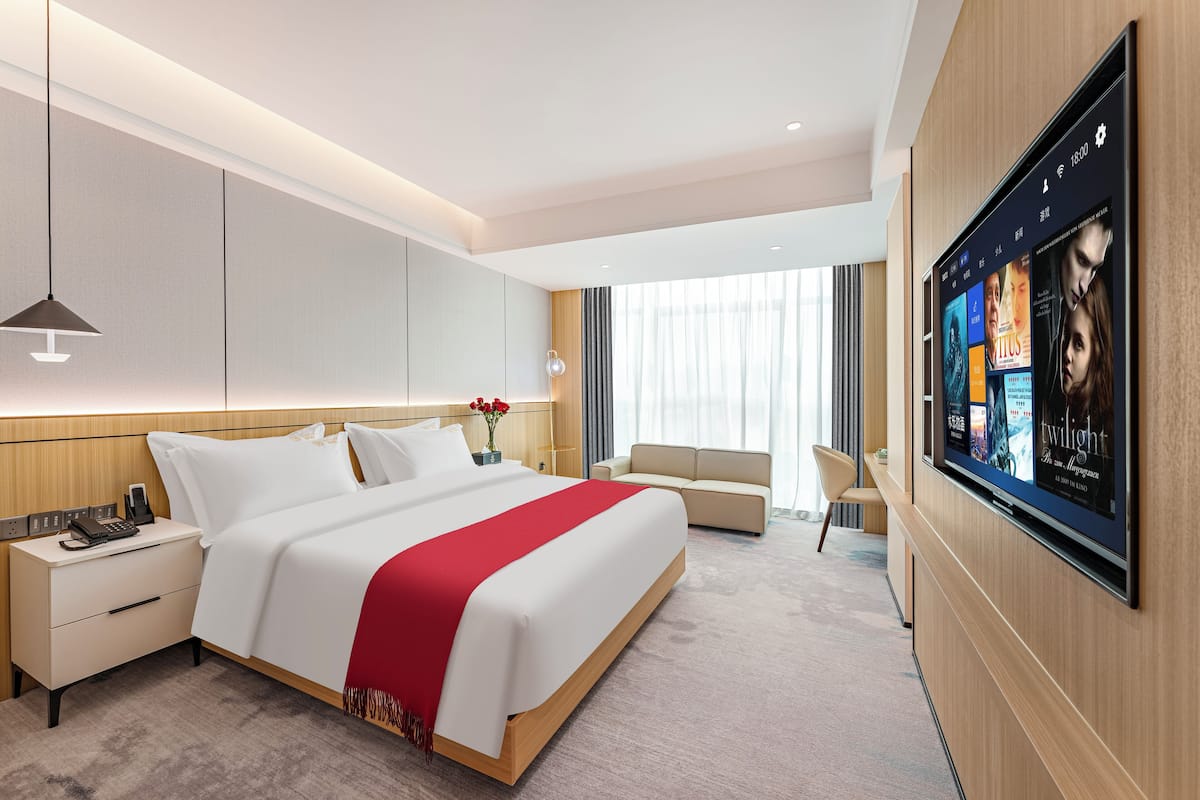 Een moderne hotelkamer met een groot bed, nachtkastjes, een flatscreen televisie en een zithoek met een bank en fauteuil.