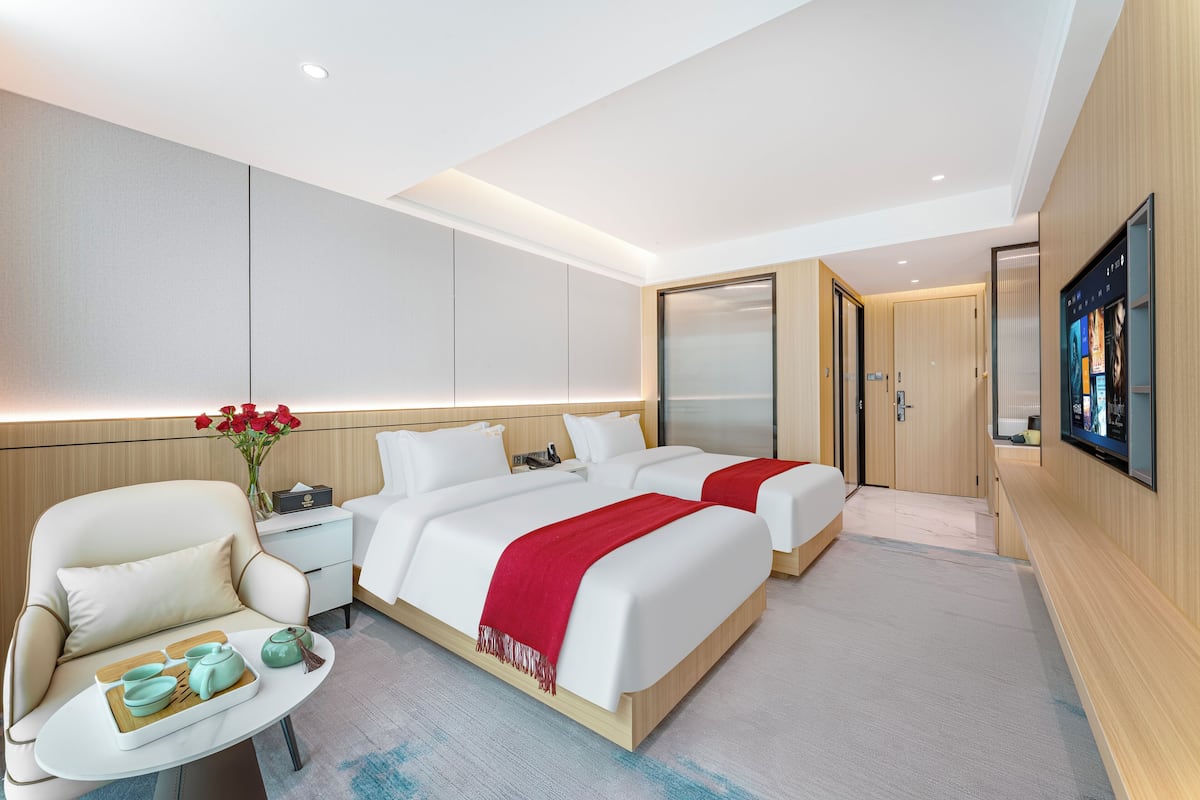 Een moderne hotelkamer met twee bedden, een zithoek, een televisie en een houten garderobe.