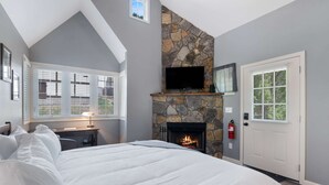 Un dormitorio con chimenea de piedra, una cama, un escritorio con lámpara y un televisor sobre la chimenea.