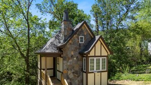 Una pequeña casa de piedra con chimenea, una escalera de madera y una ventana.